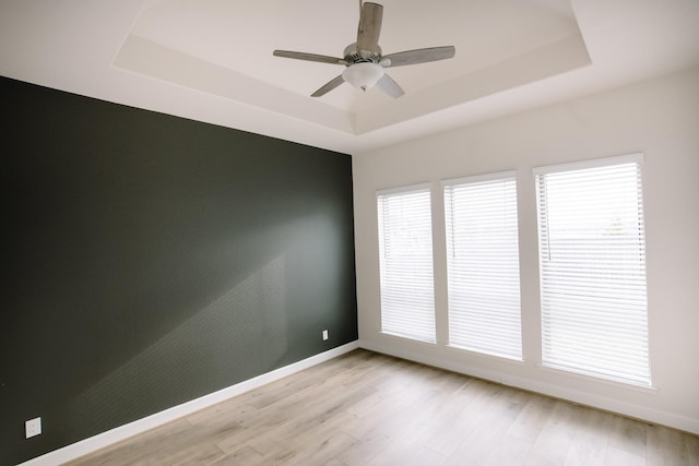 spare room with a raised ceiling, baseboards, ceiling fan, and light wood finished floors