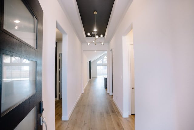 corridor with a notable chandelier, light wood-style flooring, and baseboards