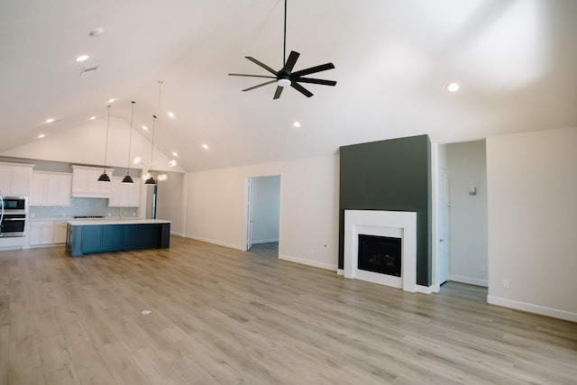 unfurnished living room with a ceiling fan, a fireplace, light wood-style flooring, and high vaulted ceiling