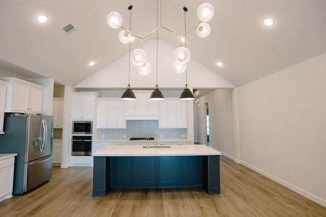 kitchen with stainless steel appliances, light countertops, decorative light fixtures, and a center island with sink