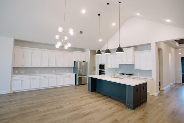 kitchen with stainless steel appliances, white cabinets, hanging light fixtures, light countertops, and a large island with sink