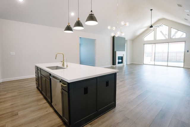 kitchen featuring open floor plan, decorative light fixtures, a kitchen island with sink, light countertops, and a sink