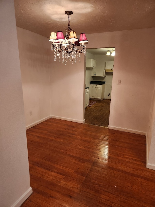 unfurnished dining area featuring a notable chandelier, dark hardwood / wood-style flooring, and a textured ceiling