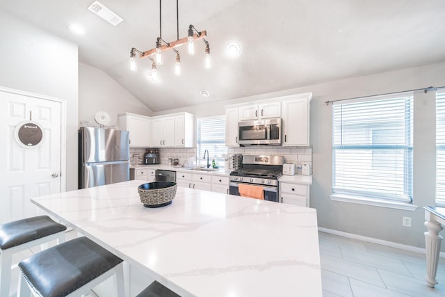 kitchen with white cabinetry, pendant lighting, lofted ceiling, decorative backsplash, and appliances with stainless steel finishes