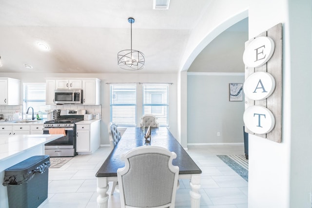 kitchen with white cabinets, stainless steel appliances, hanging light fixtures, and tasteful backsplash