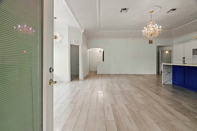 unfurnished living room with light hardwood / wood-style floors, crown molding, and a notable chandelier