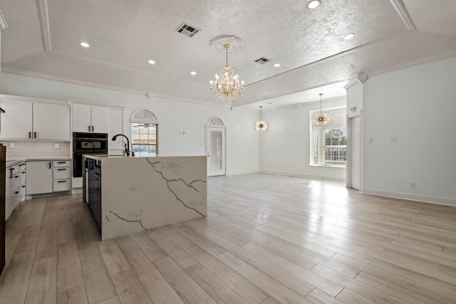 kitchen with backsplash, an inviting chandelier, white cabinets, a center island with sink, and crown molding