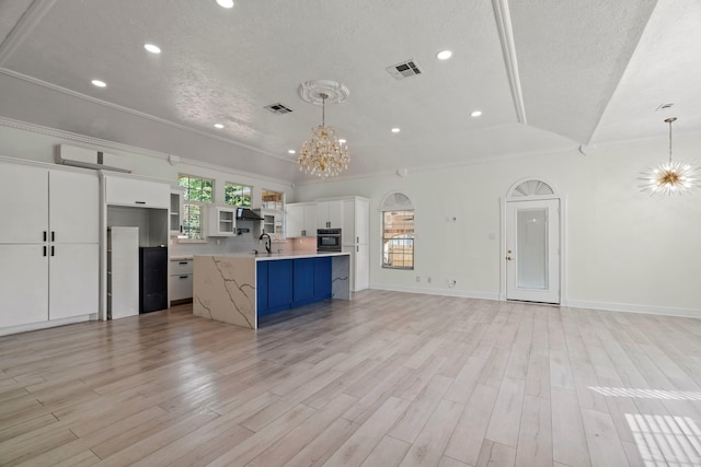 kitchen with white cabinetry, an island with sink, lofted ceiling, and an inviting chandelier