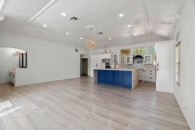 kitchen with backsplash, ornamental molding, sink, a large island with sink, and white cabinetry