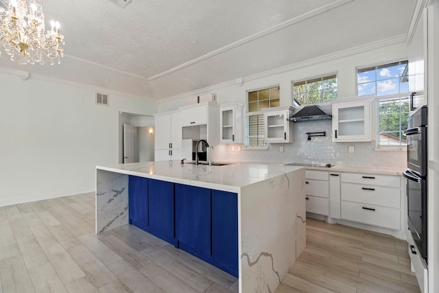 kitchen featuring white cabinets, decorative light fixtures, a center island with sink, and sink