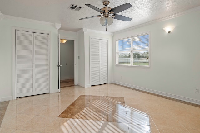 unfurnished bedroom with ceiling fan, ornamental molding, a textured ceiling, and two closets