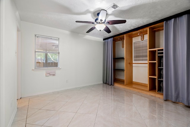 unfurnished bedroom featuring a walk in closet, light tile patterned floors, a textured ceiling, and ceiling fan