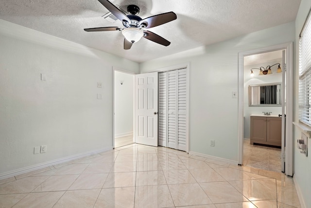 unfurnished bedroom featuring sink, ceiling fan, light tile patterned floors, a textured ceiling, and a closet