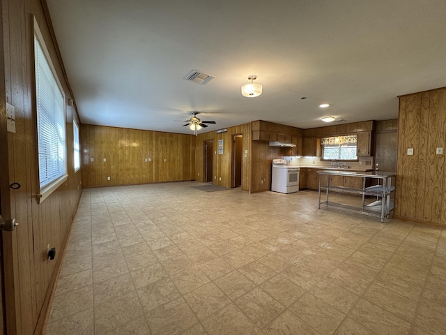 unfurnished living room featuring ceiling fan, wood walls, and sink