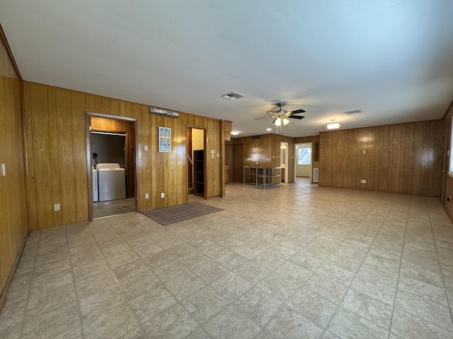 unfurnished living room with washer / clothes dryer, ceiling fan, and wood walls