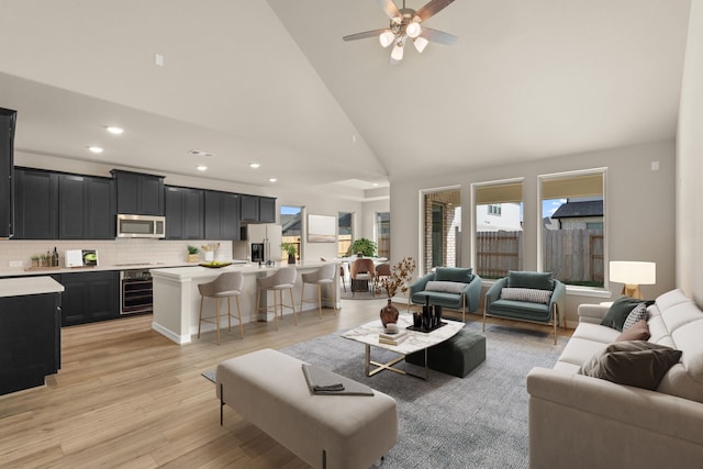 living room featuring ceiling fan, high vaulted ceiling, beverage cooler, and light wood-type flooring