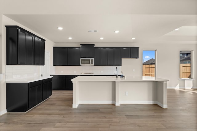 kitchen with sink, a kitchen island with sink, tasteful backsplash, and light hardwood / wood-style flooring