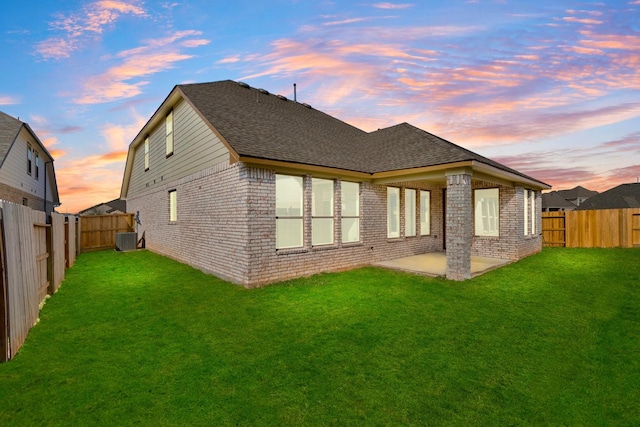 back house at dusk featuring a patio, central AC, and a lawn