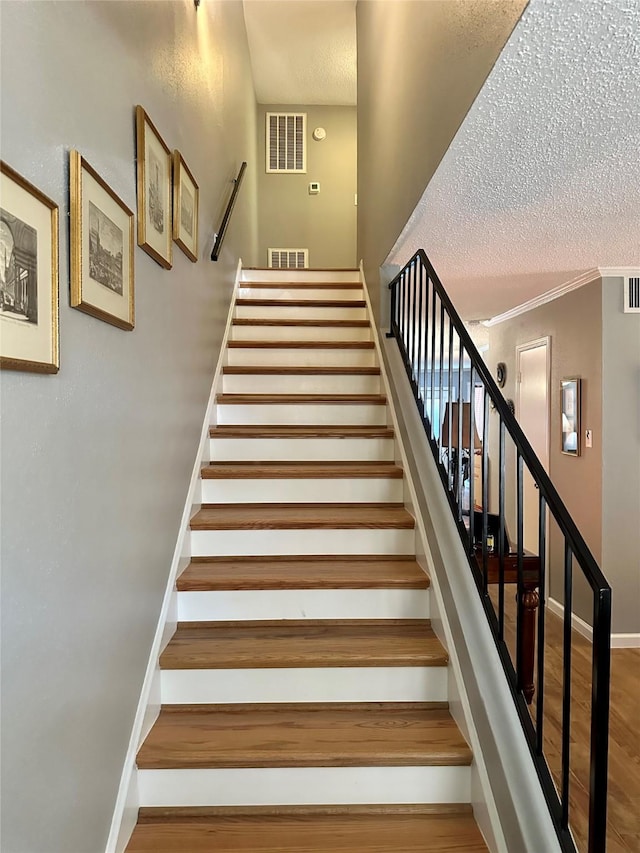 stairs with wood-type flooring, a textured ceiling, and crown molding