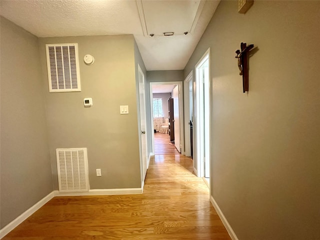 hall with light hardwood / wood-style flooring and a textured ceiling