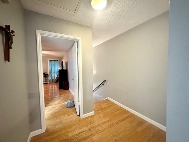 corridor with a textured ceiling and light wood-type flooring