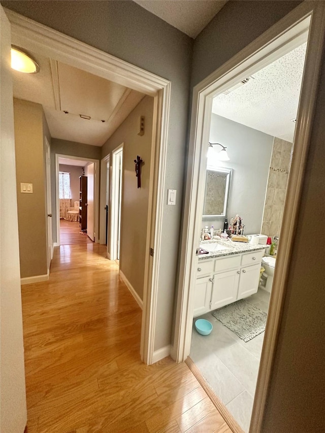 hall featuring sink, light wood-type flooring, and a textured ceiling