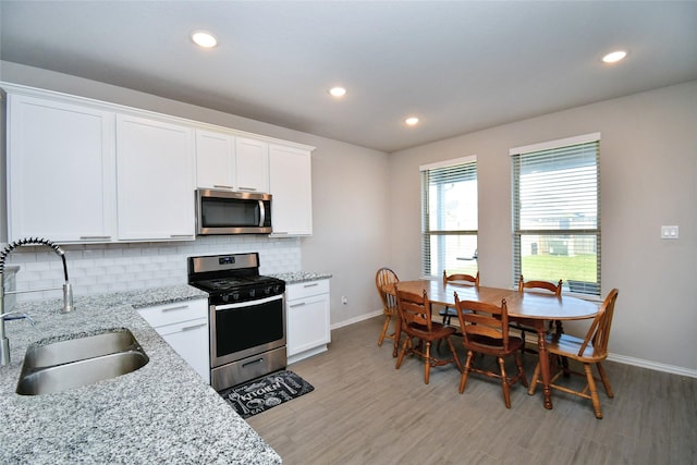 kitchen with white cabinetry, sink, light stone counters, backsplash, and appliances with stainless steel finishes