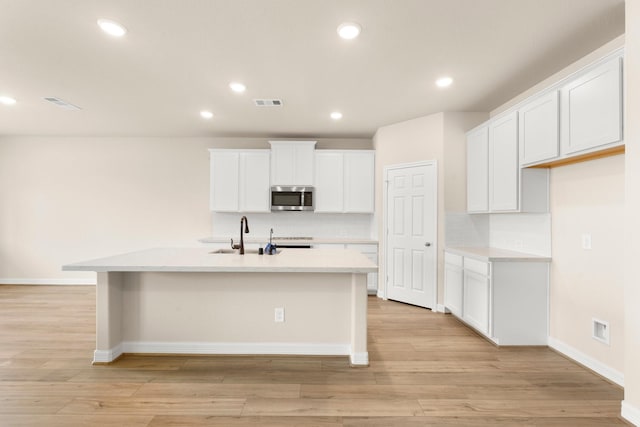 kitchen featuring backsplash, a center island with sink, white cabinetry, and sink