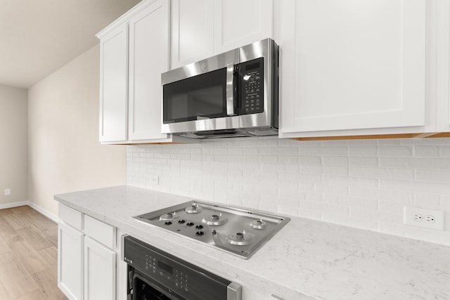 kitchen featuring light wood-type flooring, white cabinets, light stone counters, stovetop, and oven