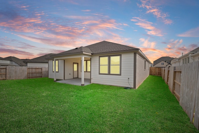 back house at dusk featuring a patio area and a lawn