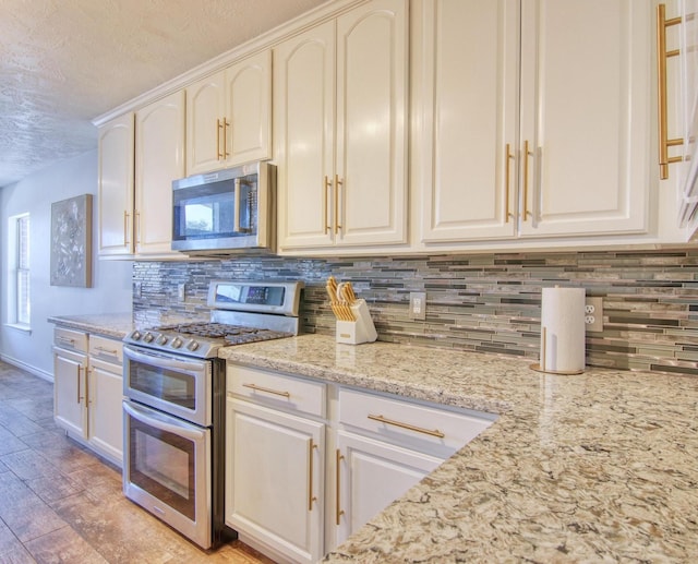 kitchen featuring light stone countertops, a textured ceiling, decorative backsplash, white cabinets, and appliances with stainless steel finishes