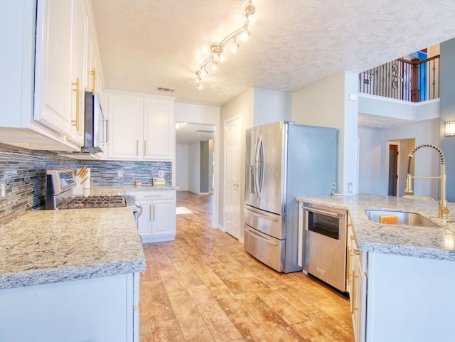 kitchen with light stone countertops, appliances with stainless steel finishes, decorative backsplash, sink, and white cabinetry