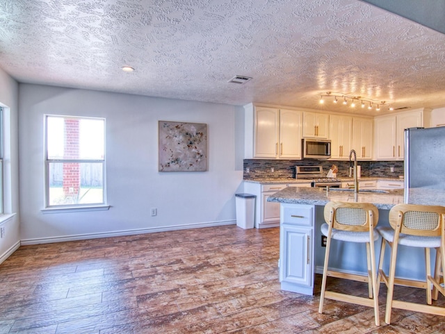 kitchen featuring a kitchen breakfast bar, tasteful backsplash, light stone counters, white cabinets, and appliances with stainless steel finishes