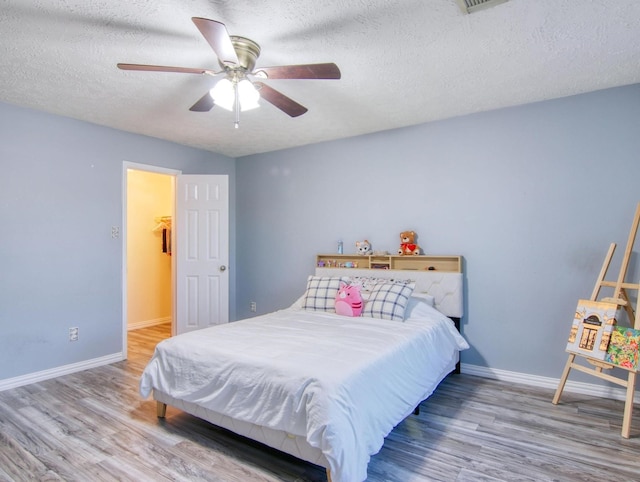 bedroom with wood-type flooring, a walk in closet, a textured ceiling, and ceiling fan