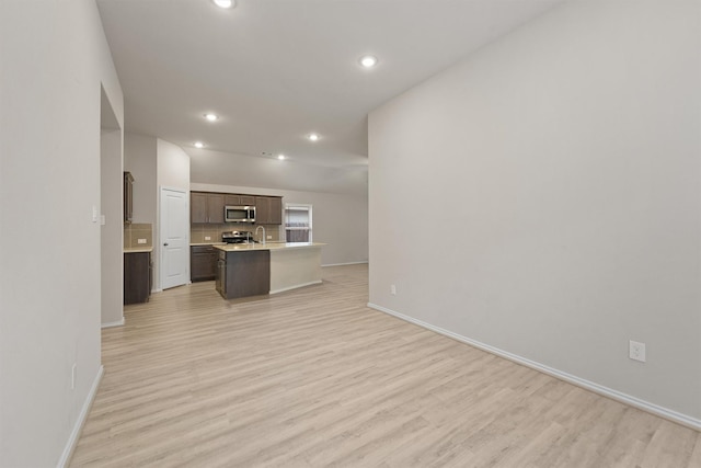 kitchen with stainless steel appliances, an island with sink, a breakfast bar area, dark brown cabinets, and light wood-type flooring