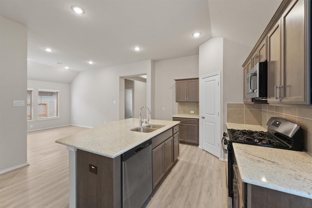 kitchen featuring decorative backsplash, light stone countertops, stainless steel appliances, lofted ceiling, and an island with sink