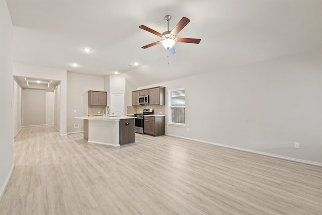 kitchen featuring sink, stainless steel appliances, lofted ceiling, a kitchen island with sink, and light wood-type flooring