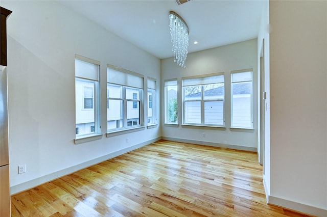 unfurnished room with a chandelier and light wood-type flooring