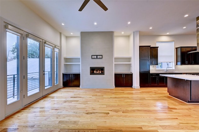 kitchen with built in shelves, ceiling fan, a large fireplace, sink, and light hardwood / wood-style flooring