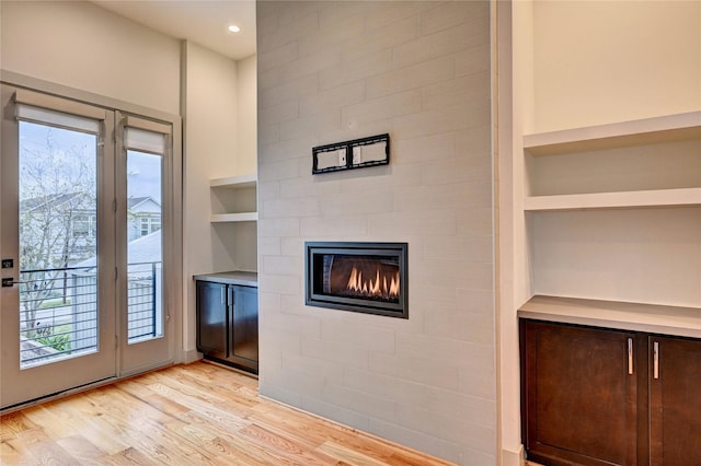 interior space with built in shelves, a tile fireplace, and light wood-type flooring