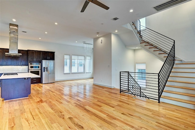 kitchen with backsplash, ventilation hood, light hardwood / wood-style flooring, and appliances with stainless steel finishes