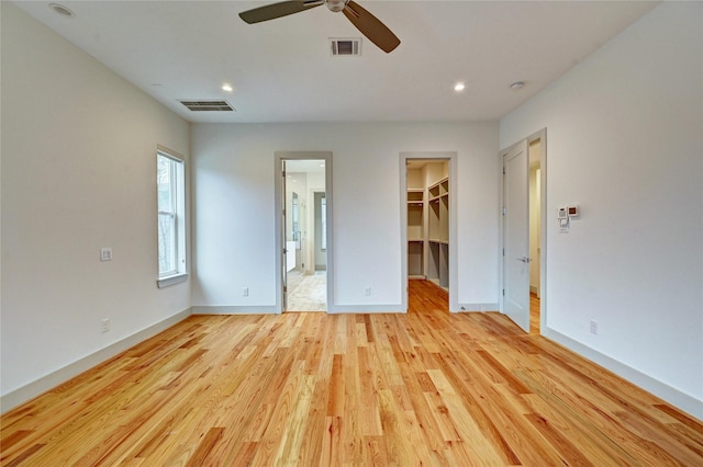 unfurnished bedroom featuring light wood-type flooring, a walk in closet, a closet, and ceiling fan