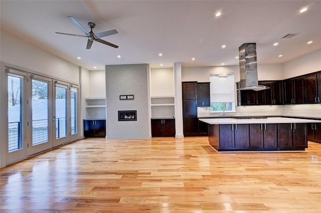 kitchen featuring island exhaust hood, decorative backsplash, a spacious island, light hardwood / wood-style flooring, and built in features