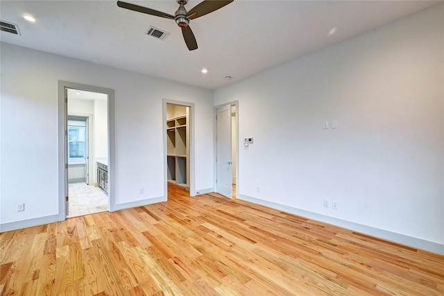 unfurnished bedroom with ensuite bathroom, ceiling fan, a spacious closet, light hardwood / wood-style flooring, and a closet