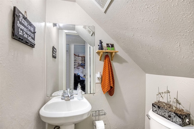 bathroom with a textured ceiling, toilet, lofted ceiling, and sink