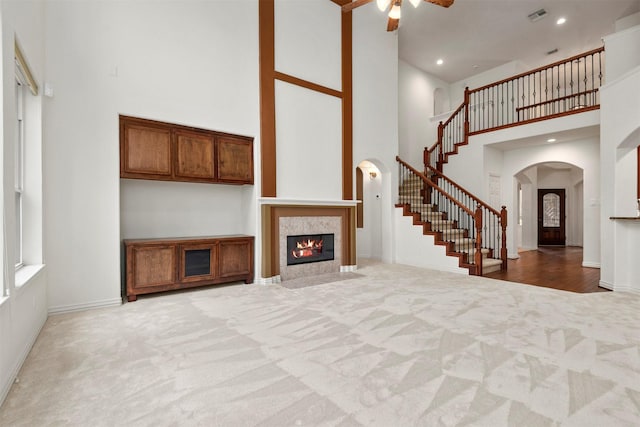 unfurnished living room with ceiling fan, light carpet, and a high ceiling