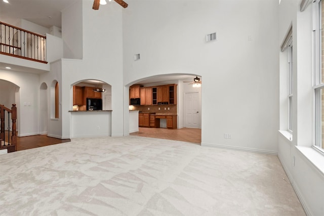 unfurnished living room with ceiling fan, light colored carpet, and a towering ceiling