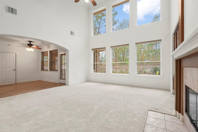 unfurnished living room featuring ceiling fan, a fireplace, a towering ceiling, and light colored carpet