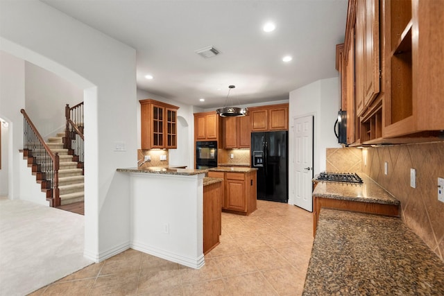 kitchen with dark stone counters, black appliances, hanging light fixtures, decorative backsplash, and light tile patterned flooring