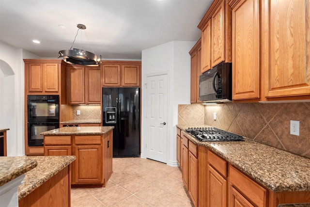 kitchen with hanging light fixtures, tasteful backsplash, light stone counters, a kitchen island, and black appliances